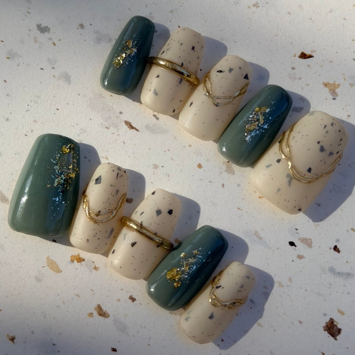 Ten medium square press-on nails in glossy sage green with gold foil and matte speckled cream with raised gold lines