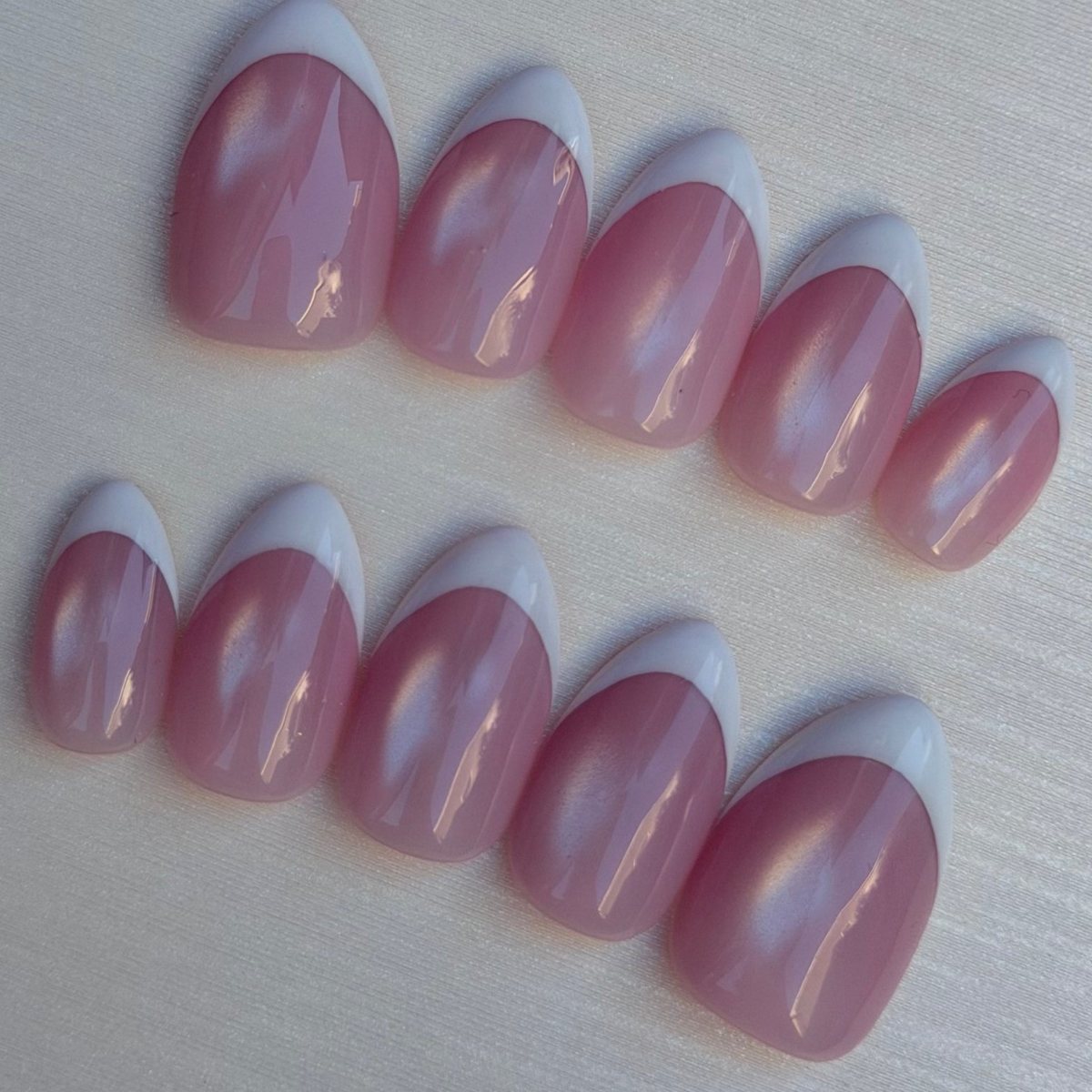 Ten short almond press-on nails in sheer pink with pearly cat-eye shimmer and white French tips