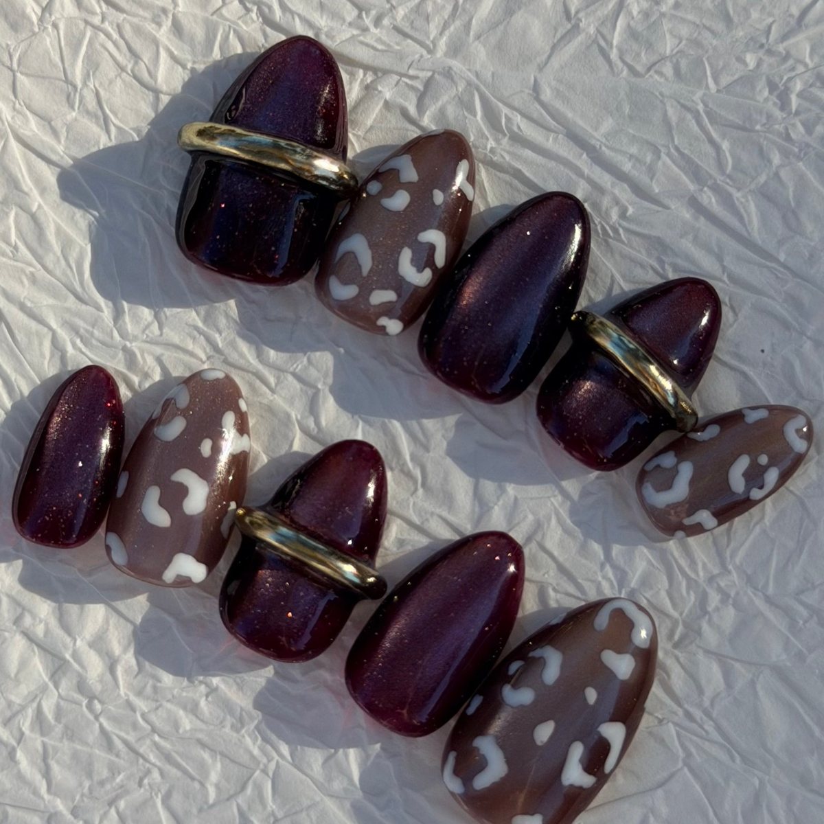 Ten short almond press-on nails in deep plum velvet cat-eye and cocoa with cream leopard spots and raised gold cuffs